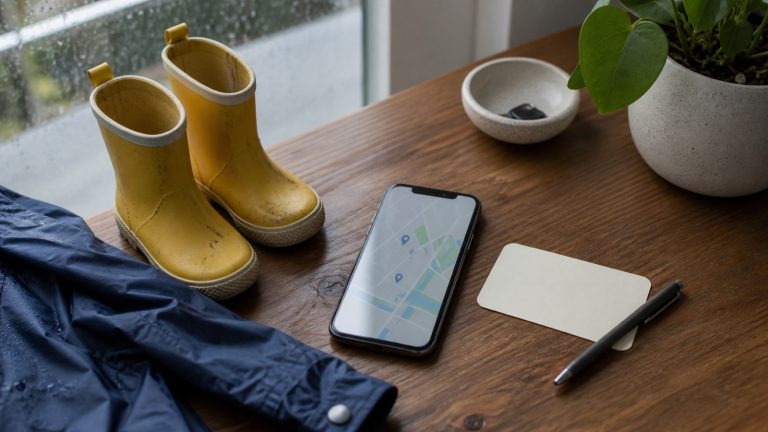 Small rain boots, a phone and a blank appointment card arranged for a Vancouver pediatric care search